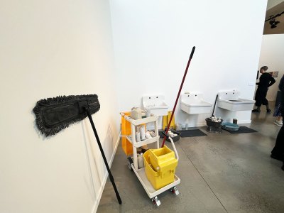 An installation consisting of various objects in porcelain: three sinks, rolls of toilet paper, a janitor's cart with cleaning supplies, and more.
