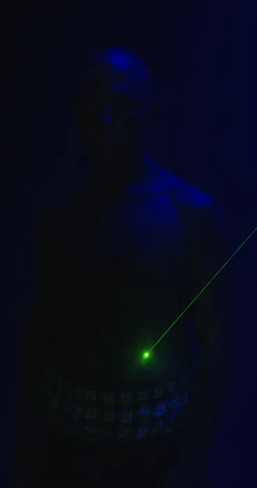 A person in a dark blue space with a green laser aimed at their stomach.