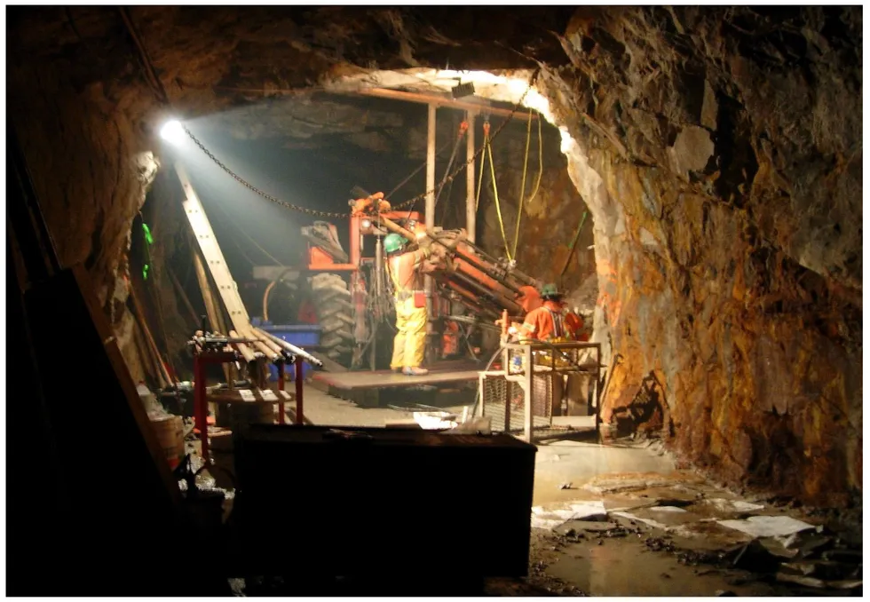 Miners operating machinery in a dimly lit underground tunnel during a drilling program at Apex Resources' Jersey-Emerald project