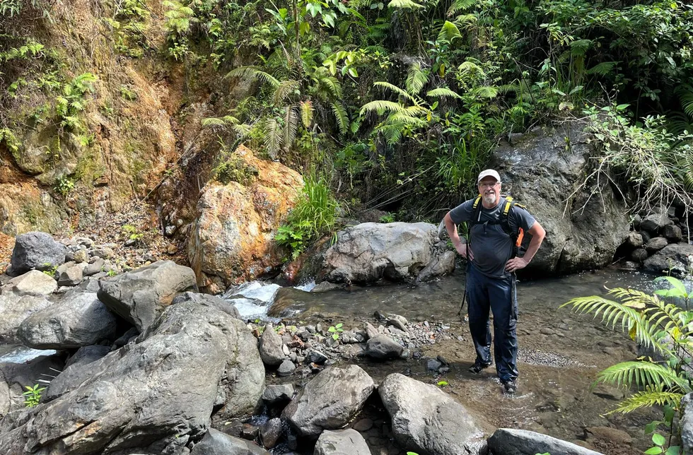 Sankamap Metals CEO John Florek investigating in a rocky stream amidst lush greenery and boulders.