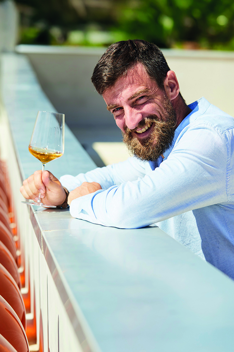 Antoine Arraou leaning on wall with a glass of wine